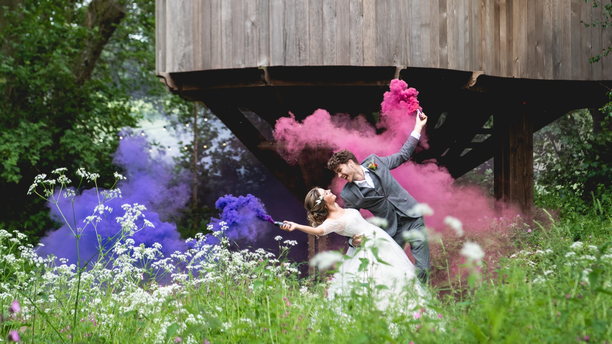 Married man and woman dancing holding pink and purple smoke bombs outside