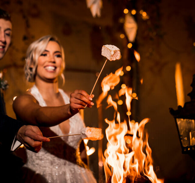 Happy smiling newly married couple toasting marshmallows over mini bonfire